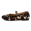 A single women's flat shoe with a brown, black, and cream cowhide pattern, featuring a Mary Jane strap with a small gold buckle, shown against a plain white background.